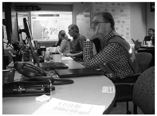 The figure is a photo of workers at the Oregon Public Health Agency Operations Center during the 2009 H1N1 influenza pandemic.  
